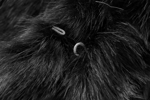 Close-up of black faux fur texture with delicate woven loop closure detail