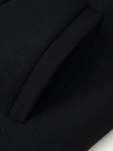 Close-up of the detailed pocket craftsmanship and textured black wool fabric on this coat