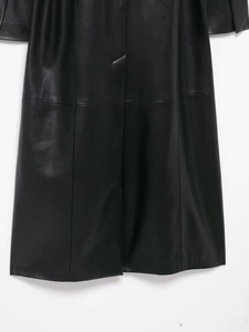 Détail d'un long manteau noir en simili cuir montrant la texture lisse et les coutures