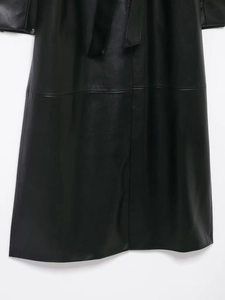 Détail du manteau long en similicuir noir avec coutures fines et ceinture à la taille