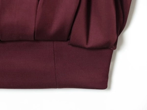 Dettaglio del tessuto bordeaux plissettato con cuciture sottili e texture opaca