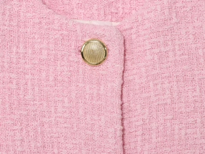 Dettaglio della trama in tessuto tweed rosa con un bottone metallico dorato rotondo