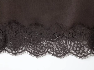 Detail of deep brown satin hem featuring intricate black eyelash lace floral trim