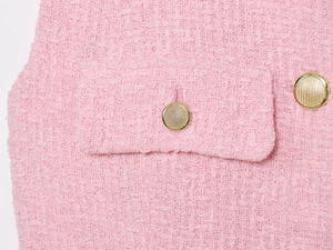 Dettaglio del tessuto in tweed rosa con bottoni dorati decorativi e tasca applicata