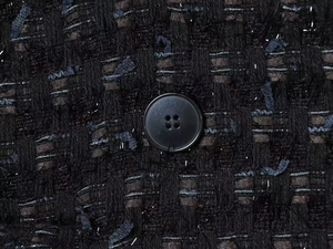 Detailed close-up of dark tweed fabric texture with silver glitter and a black button