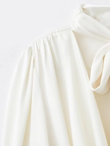 Détail d'un chemisier en satin blanc perle avec épaules plissées et nœud élégant au col