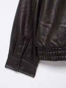 Détail d'une veste en similicuir marron foncé avec texture grainée, bouton et ourlet élastique