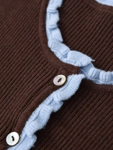Detail of ribbed knit fabric with ruffled trim and pearlescent buttons on a contrast cardigan