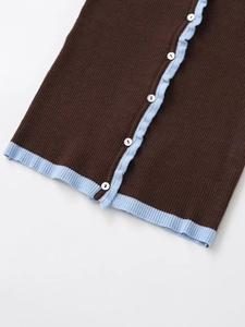 Detail of dark brown knit cardigan with light blue trim and white buttons on a clean surface