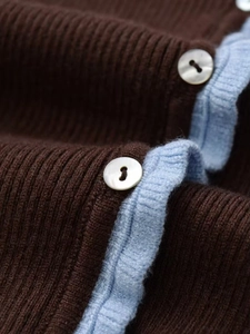 Detailed macro view of dark brown ribbed knit cardigan with contrast blue trim and pearl buttons