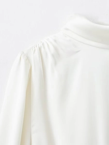 Détail du chemisier en satin blanc avec plis aux épaules et col montant très élégant
