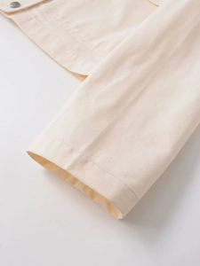 Close-up of beige twill jacket cuff with silver metal button and double-stitched details