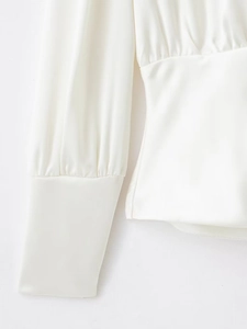 Détail de la manche d'un chemisier en satin blanc avec poignet raffiné et texture soyeuse