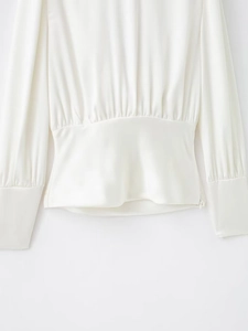 Détail de la blouse blanche en satin à manches longues avec plis à la taille et lustre