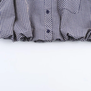 Detail of blue and white gingham shirt with dark navy buttons and pleated hem design