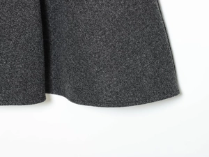 Detail of charcoal grey wool-blend fabric texture and flat hem on the poncho jacket