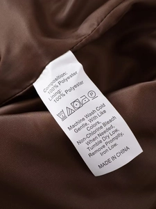 Macro shot of 100% polyester care label and washing instructions on a brown jacket