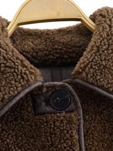 Detailed macro view of brown faux shearling jacket collar with dark leather trim and button