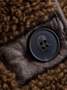 Close-up of black button on brown plush faux fur fabric with leather detail base