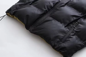 Détail d'un gilet matelassé noir brillant avec doublure verte et fermeture éclair