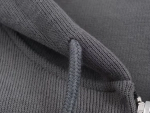 Macro detail of dark grey ribbed knit fabric with woven drawstring and metal zipper