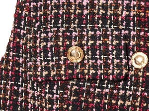 Detailansicht von strukturiertem Tweed-Stoff mit einem polierten Goldknopf und Taschennaht