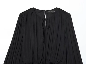 Detail of black long-sleeved dress showing pleated texture and drawstring neck cutout