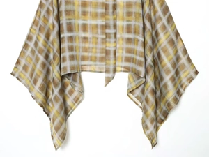 Detailed view of yellow and brown plaid fabric texture and fringed hem of a poncho top