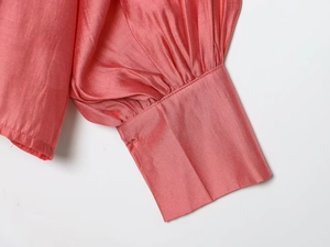 Detail of coral satin blouse showing pleated lantern sleeve cuffs and glossy silk texture