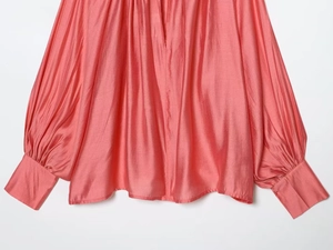 Detail of pink satin blouse sleeve showing smooth silk texture and wide cuff stitching