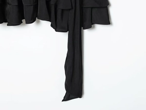 Detail of black silky dress fabric featuring layered ruffles and long waist tie strings