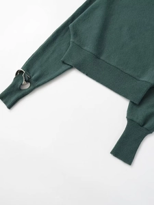 Detail shot of dark green knit sweater featuring ribbed cuffs and silver metal ring accents