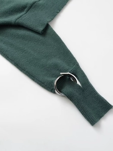 Detail of dark green knit fabric featuring hollow-out design and silver metal rings