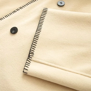 Close-up of minimalist beige wool coat with black blanket stitch and round buttons
