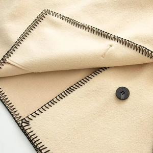 Detailed view of beige wool coat with decorative black whipstitch edges and button