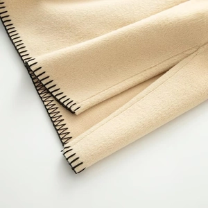 Macro shot of minimalist beige wool coat fabric with detailed black contrast stitching