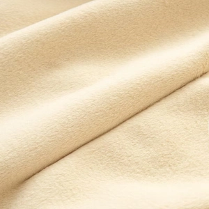 Close-up of soft cream-colored plush fabric texture on a long-sleeved winter coat
