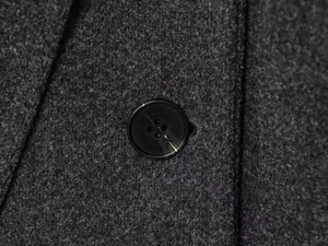 Macro detail of dark grey wool coat featuring a marbled black four-hole resin button