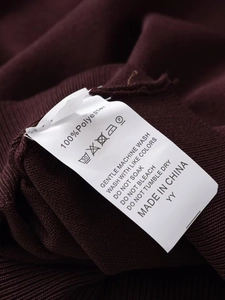 Close-up of garment care label showing 100% polyester material on red knit fabric