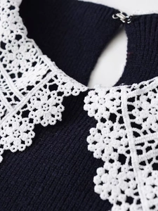 Detail of navy blue knitwear with intricate white lace collar and metal hook closure