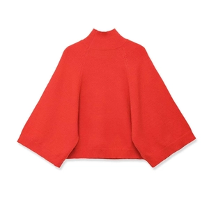 Detail of red turtleneck poncho sweater featuring wide sleeves and ribbed texture