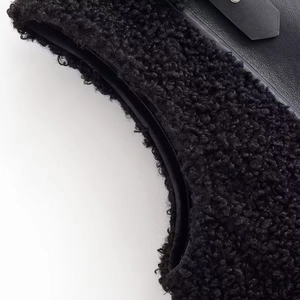 Détail de gilet en peau lainée noire avec sangle à boucle en cuir et texture peluche