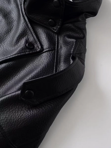Detail of black leather jacket showing grainy texture, metal snap buttons, and lapel