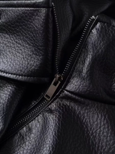 Detail shot of black pebbled leather texture and dark silver metal zipper on jacket