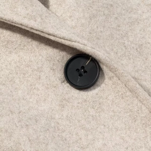 Detailed macro shot of a black four-hole button on soft oatmeal wool coat fabric