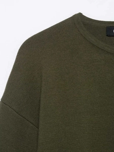 Detail view of olive green knit sweater showing round neck and smooth texture fabric