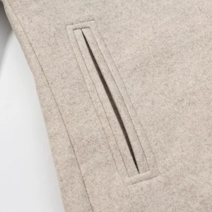 Detail shot of a minimalist beige coat featuring high-quality welt pocket and wool texture