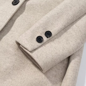 Detail of beige wool coat sleeve showing fine texture and black round button closure