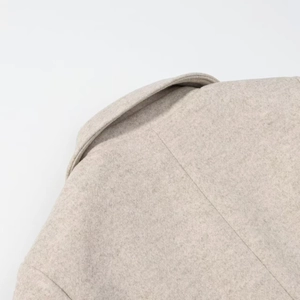 Close-up of oatmeal wool coat fabric texture and fine stitching detail on shoulders