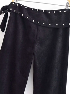 Detail of high-waist black suede trousers with silver studs and tie-up bow belt